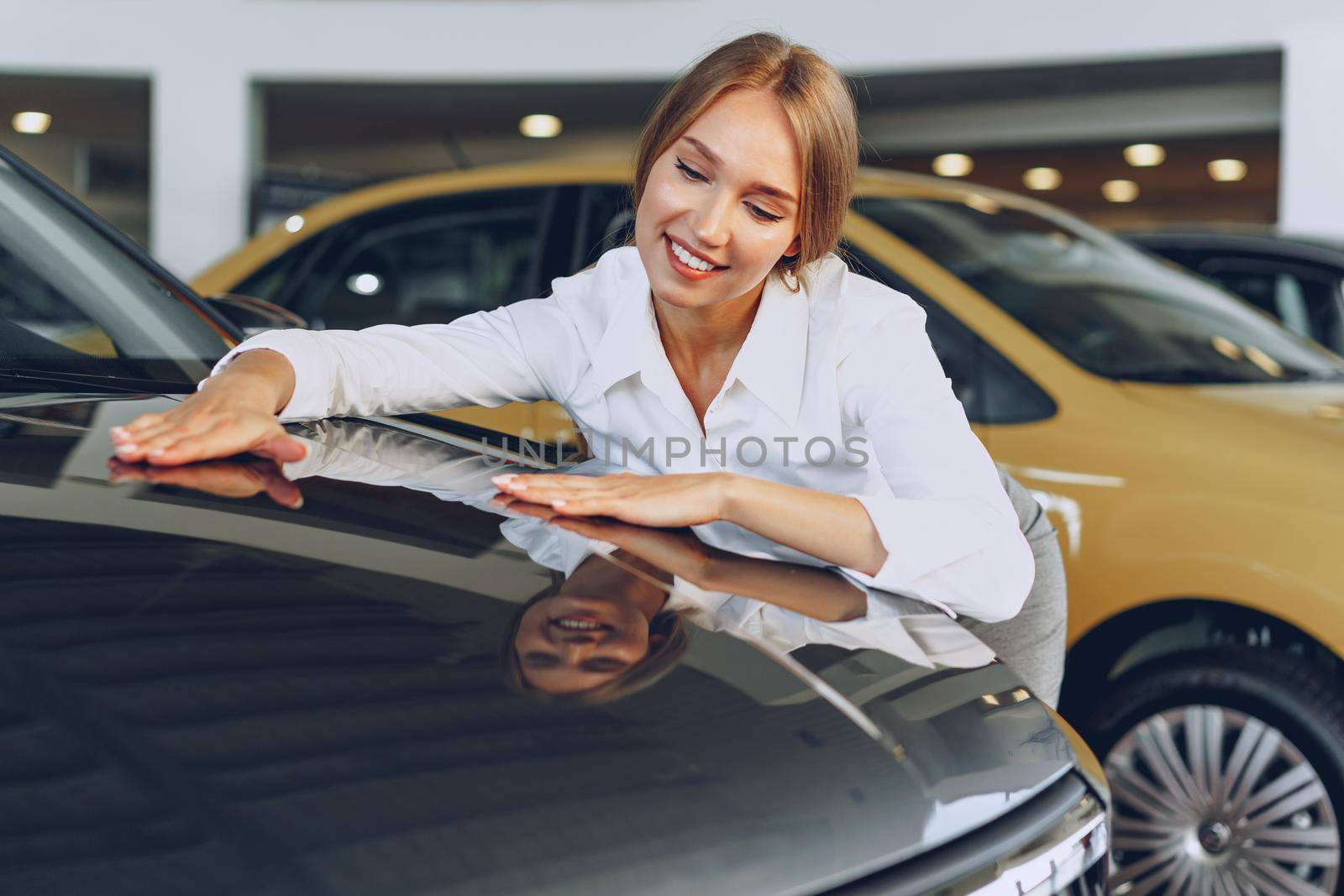 Beautiful young woman touching her new car with pleasure and joy