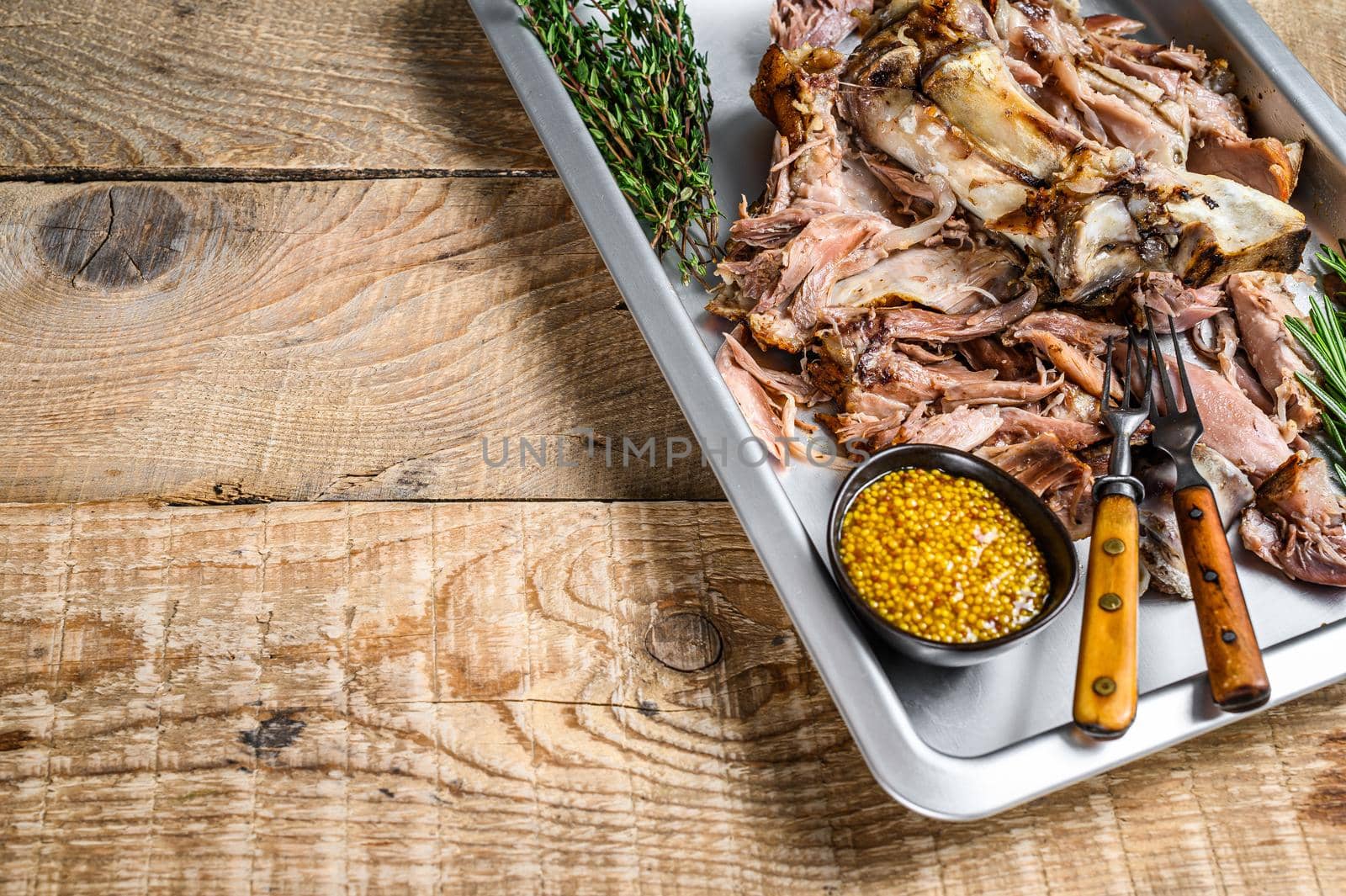 Baked pork knuckle eisbein meat on a baking pan with herbs. Wooden background. Top view. Copy space by Composter