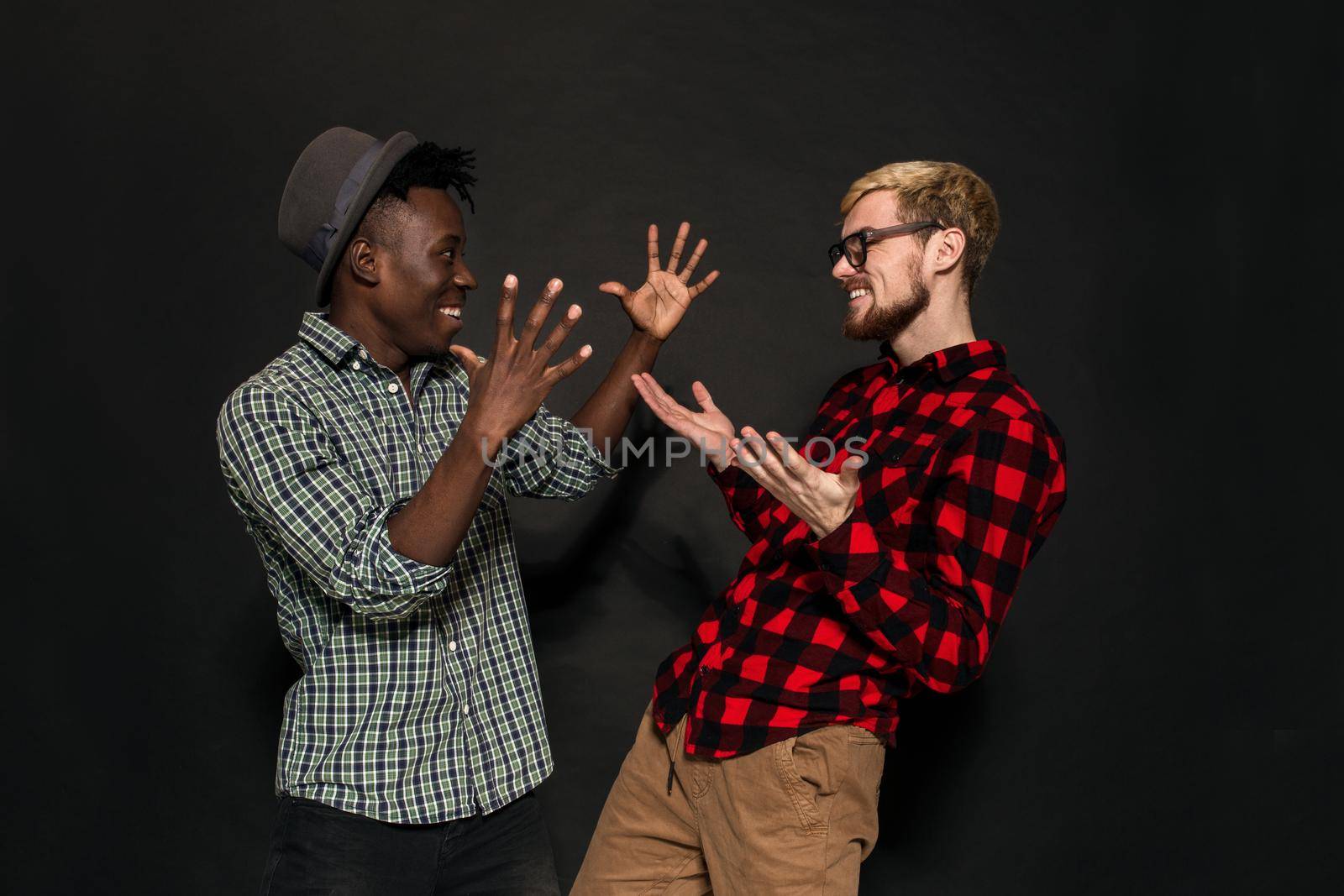 A Friend portraits shot against dark background. Two best friends are posing and having fun in the studio. Dressed in casual clothes, shirts in a cage.