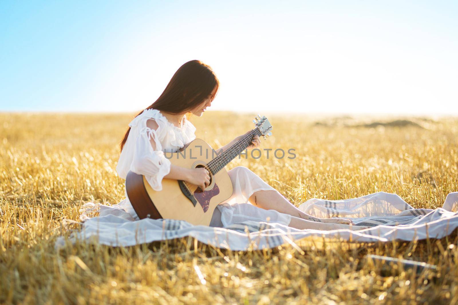 Summer is a great dream time. Beautiful girl playing the guitar in a wheat field .