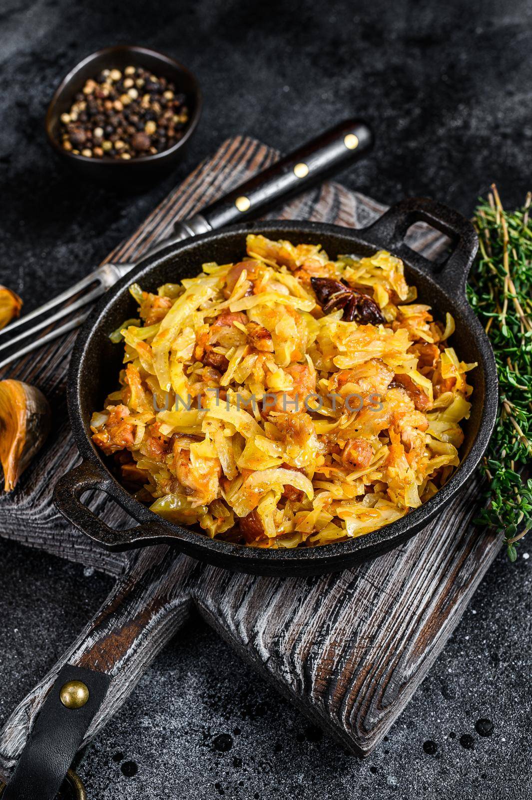 Stewed cabbage Bigos with mushrooms and sausages. Black background. Top view by Composter