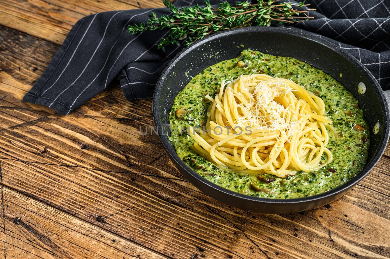 Pasta spaghetti with pesto sauce and fresh spinach and parmesan in a pan. Wooden background. Top view. Copy space.