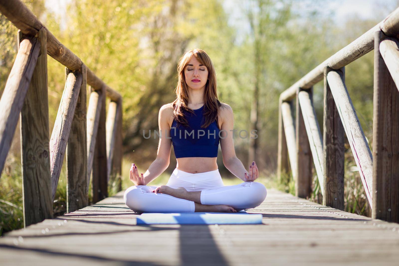 Young woman doing yoga in nature. Female wearing sport clothes in lotus figure.