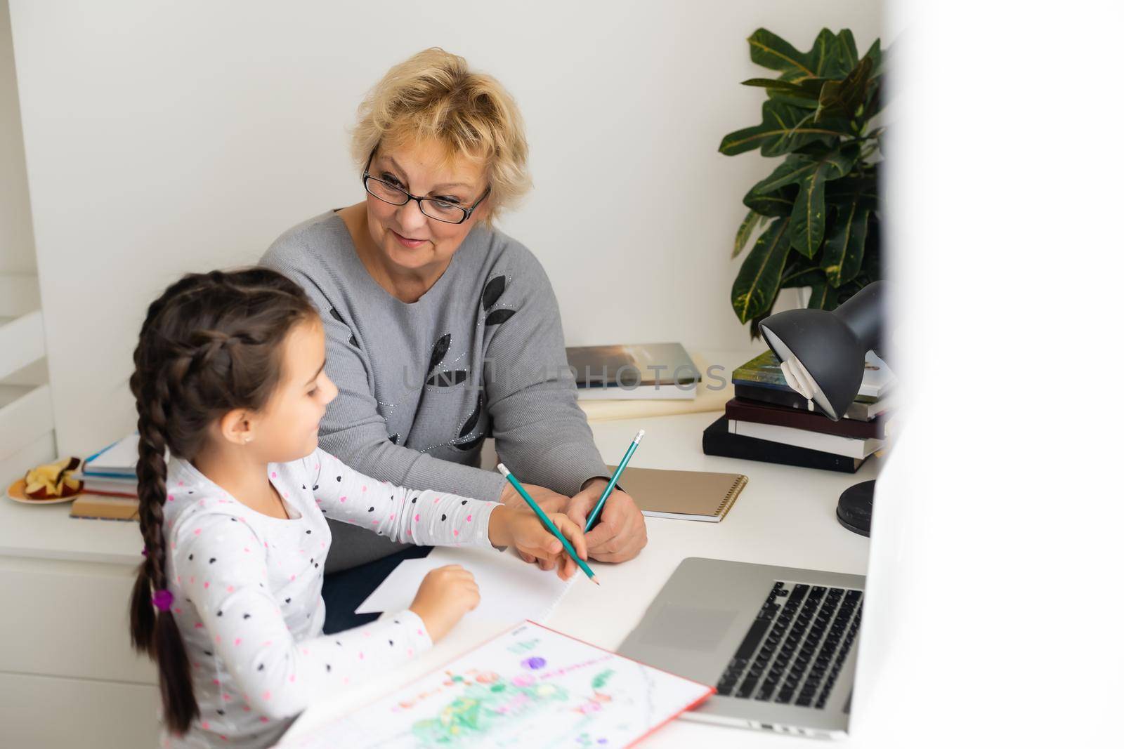 Cute and happy little girl child using laptop computer with her grandma, studying through online e-learning system. by Andelov13