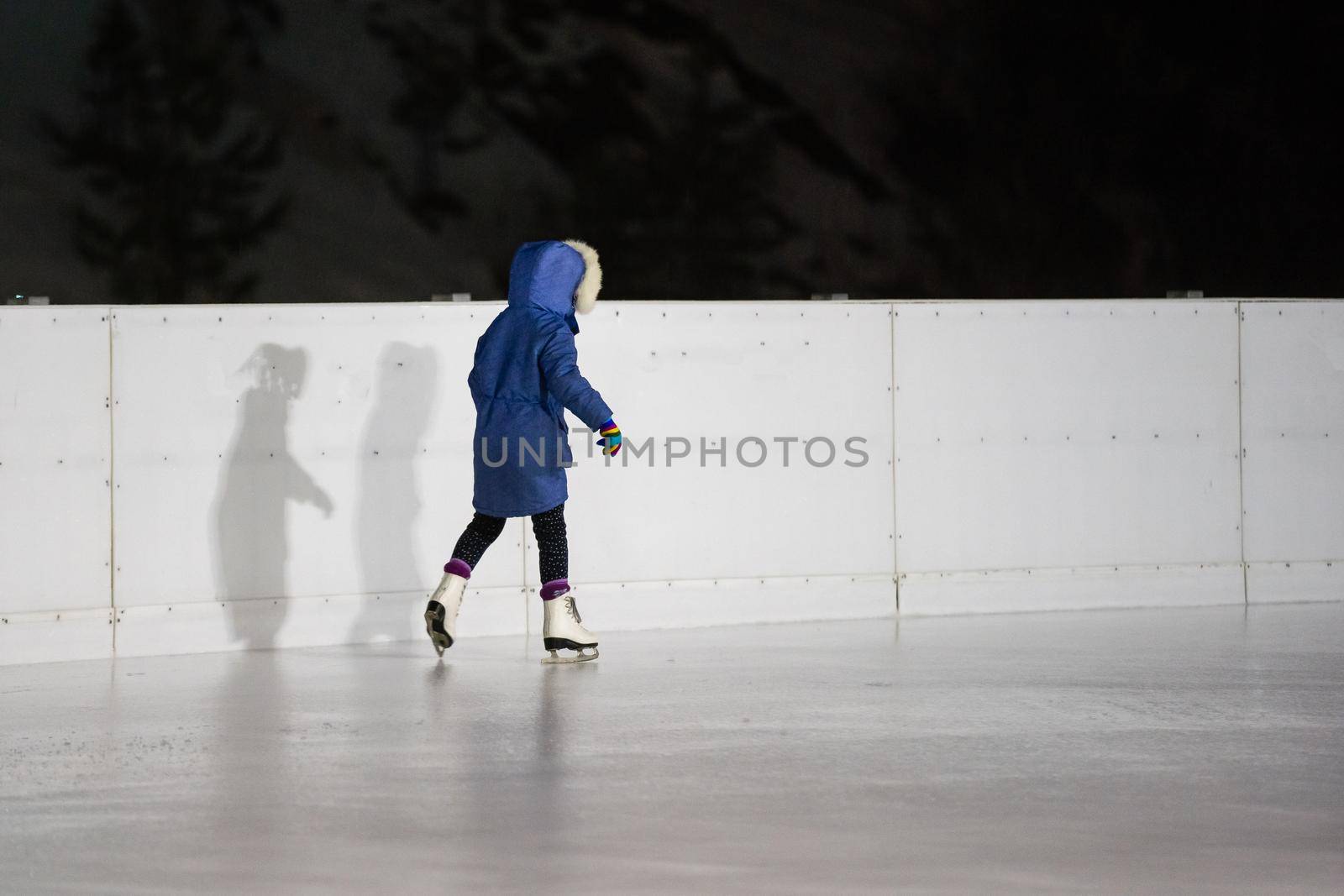 Cute little girl ice skating on a rink in the city center