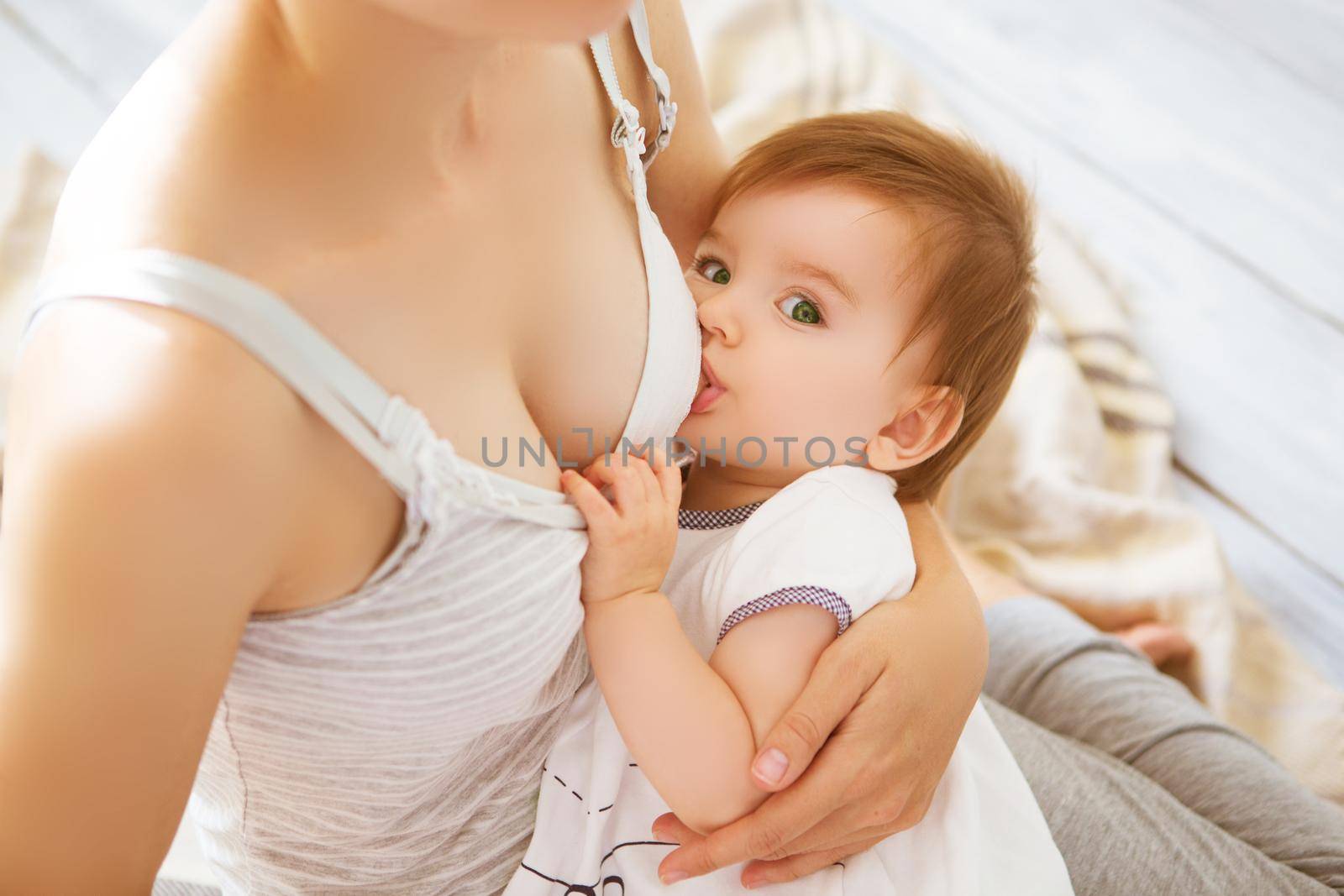 Young mother holding her newborn child. Mom nursing baby in a white bedroom. Nursery interior. Family at home.
