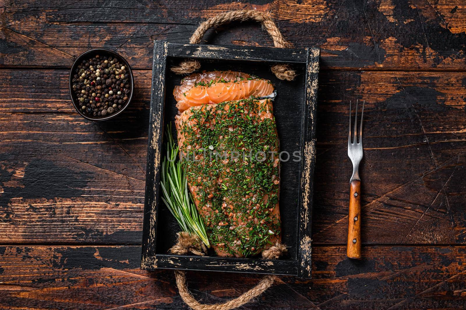 Salmon Gravlax cured with dill and salt in wooden tray. Dark wooden background. Top view.