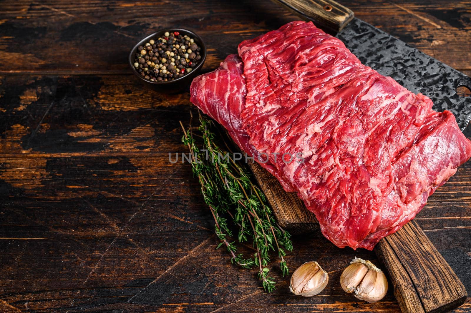 Big piece of raw beef brisket cut meat with herbs and butcher cleaver. Dark wooden background. Top view. Copy space.