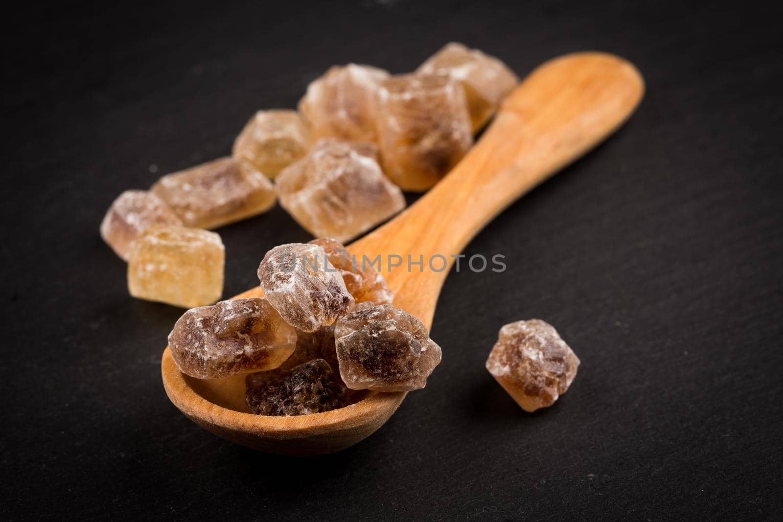 caramelized candy brown sugar in wooden spoon on a dark stone board