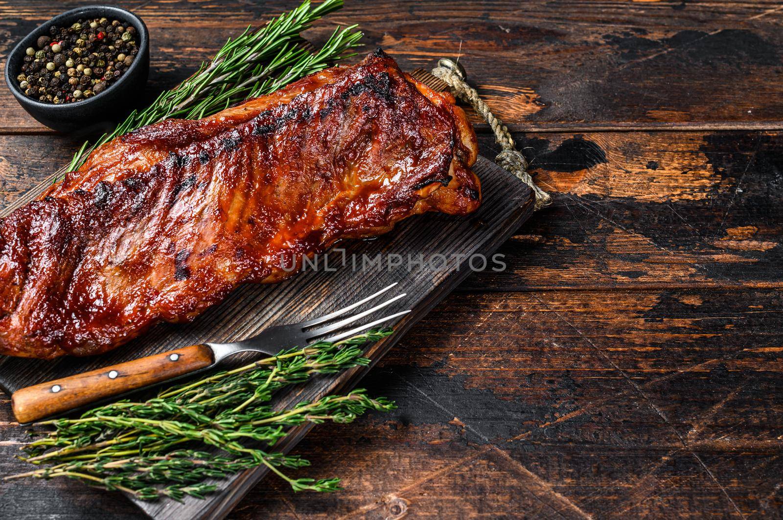 BBQ grilled veal calf brisket meat on short spare rib on wooden cutting board. Dark wooden background. Top view. Copy space.