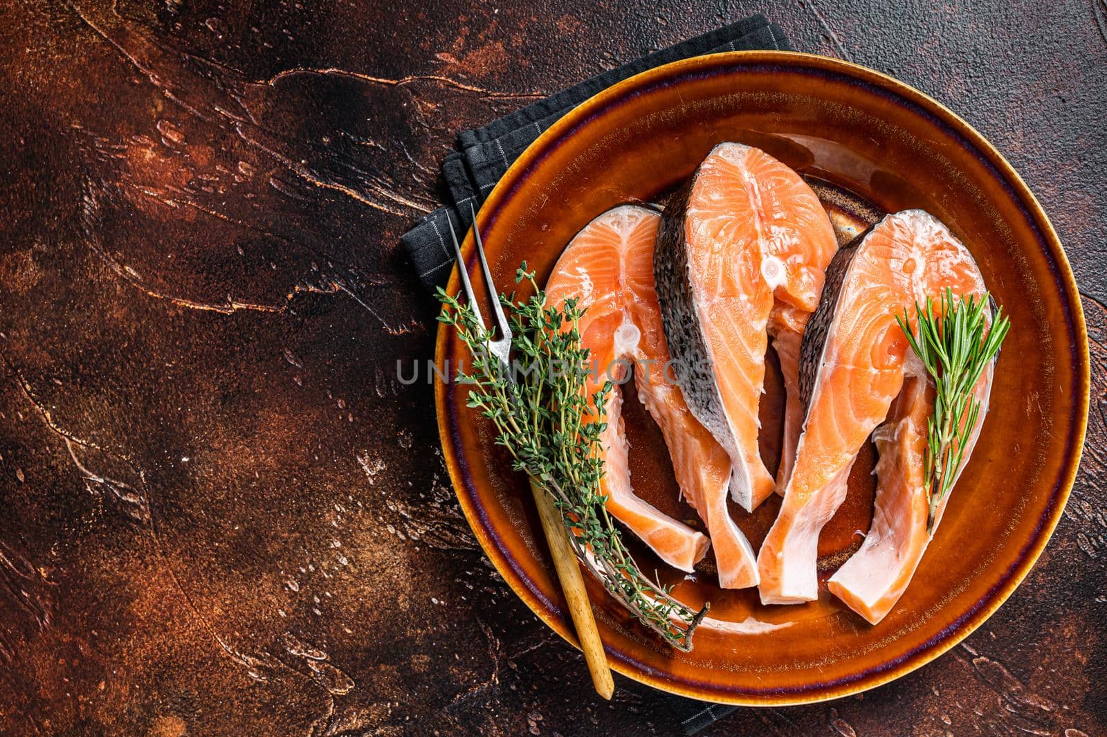 Salmon raw steaks on rustic plate with herbs. Dark background. Top view. Copy space by Composter
