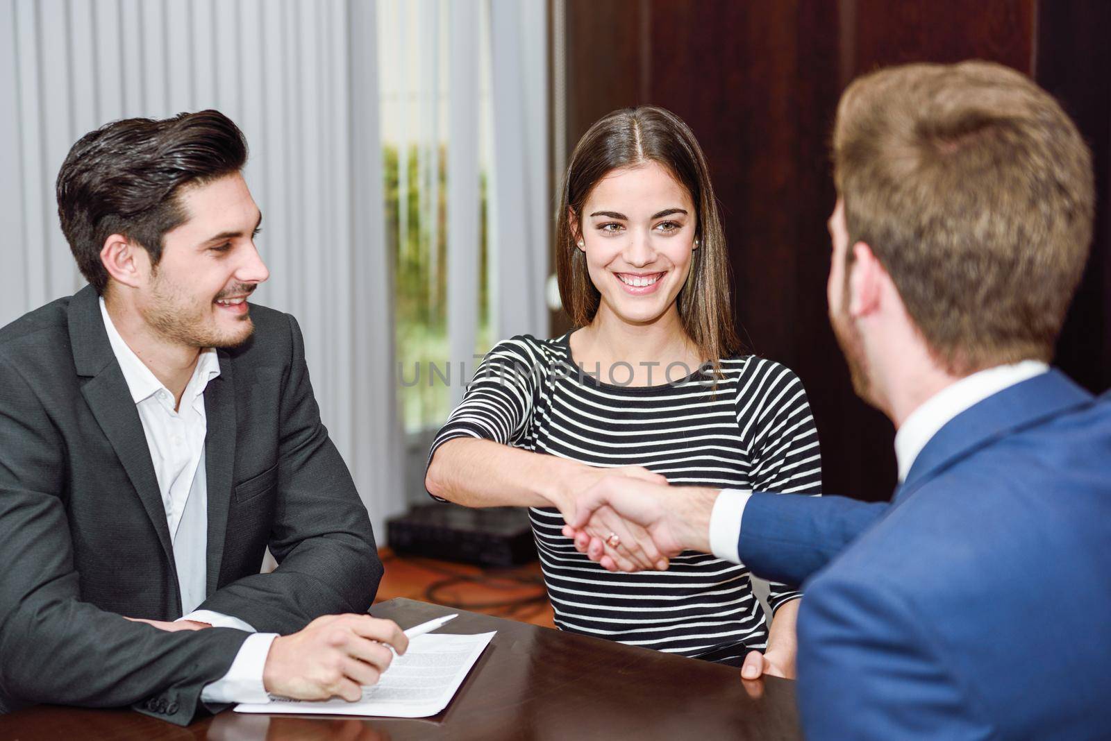 Smiling young couple shaking hands with an insurance agent by javiindy