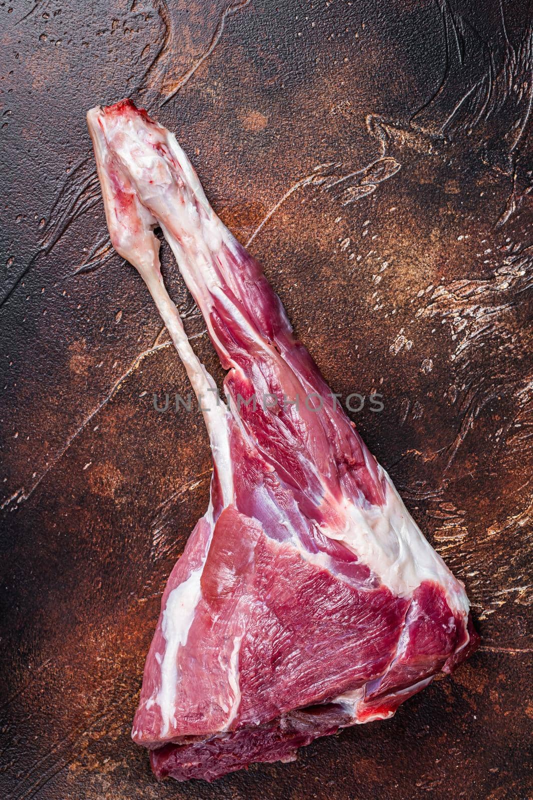 Whole raw lamb leg meat on the bone. Dark background. Top view.