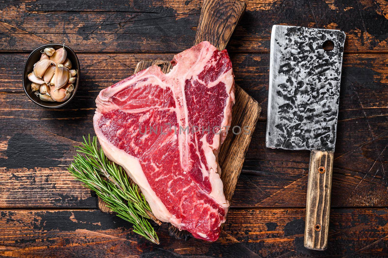Italian Florentine T-bone beef meat Steak with herbs on a wooden cutting board. Dark wooden background. Top view.