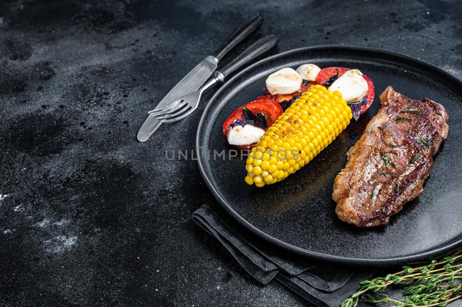 Roasted P beef steaks Striploin or New York on a plate with garnish. Black background. Top view. Copy space.