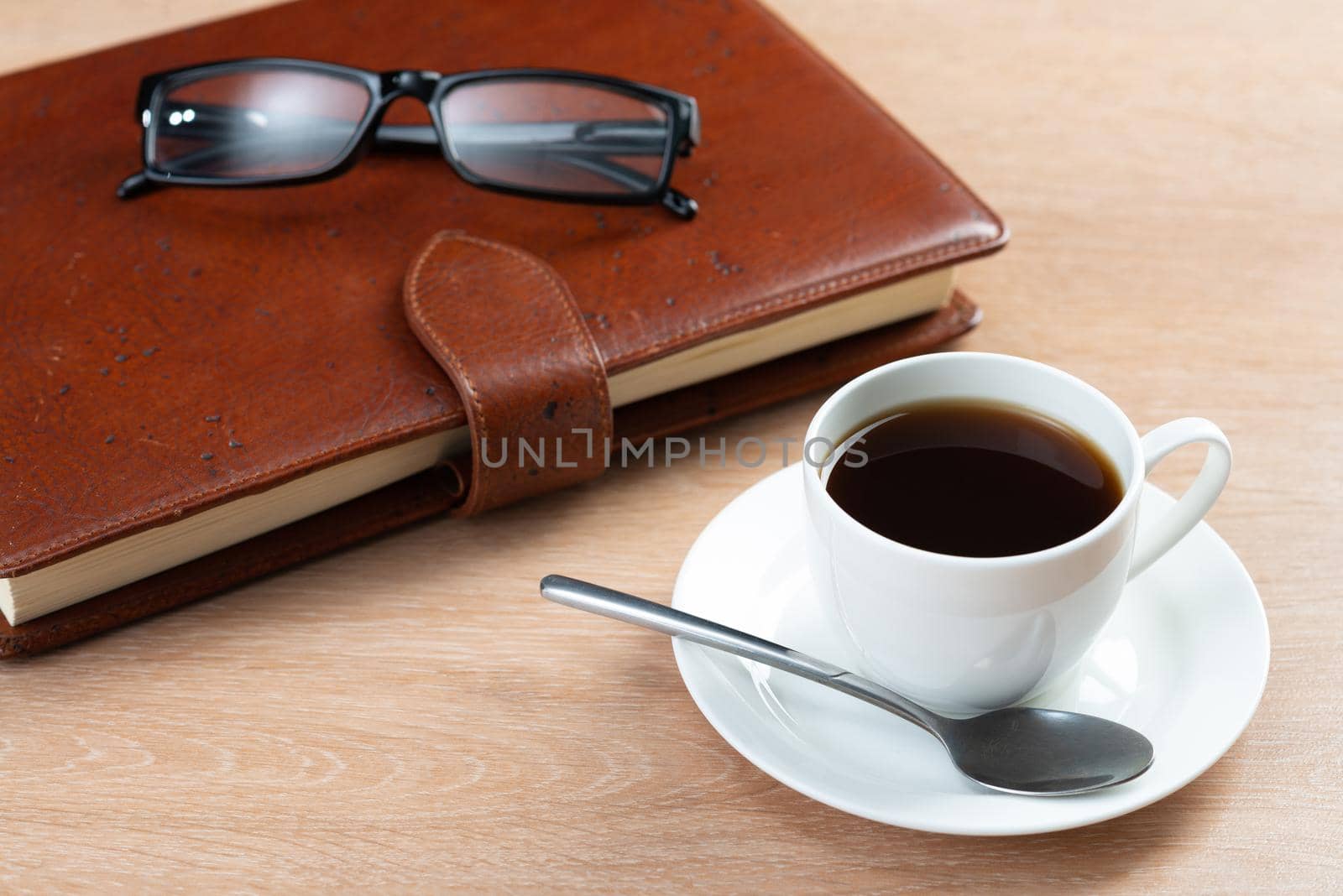 Brown leather notebook and glasses on wooden table. Businessman workspace with cup of black coffee. Business planning and work day organization. Coffee break at workplace in office.