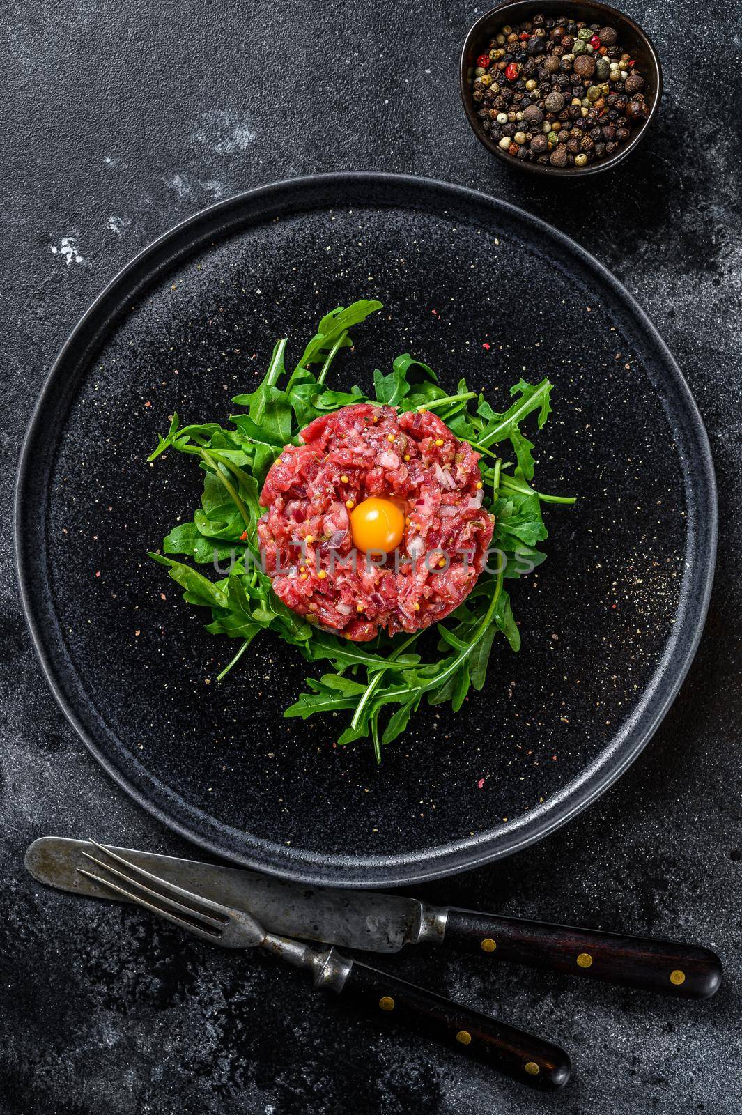 Beef tartar with a quail egg served on a black stone plate.. Black background. Top view by Composter