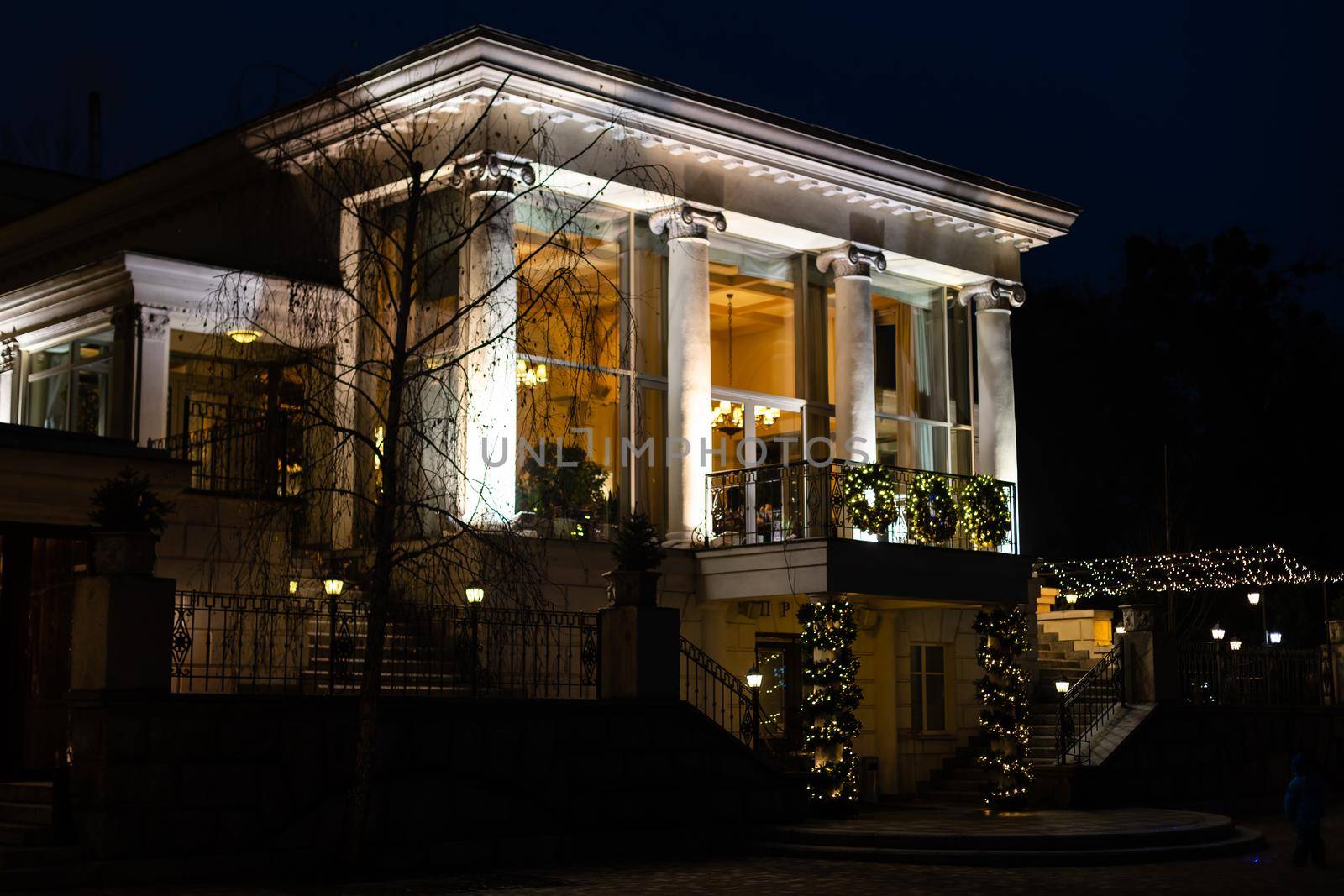 lantern of cafe lighting glowe with warm light in the night garden of the backyard in the background bokeh balls from garland on the facade restaurant building, nobody. by Andelov13