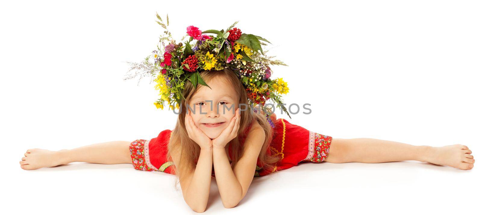 Adorable little girl in a bright red dress with a large floral wreath on his head. Girl does the splits-Isolated on white background
