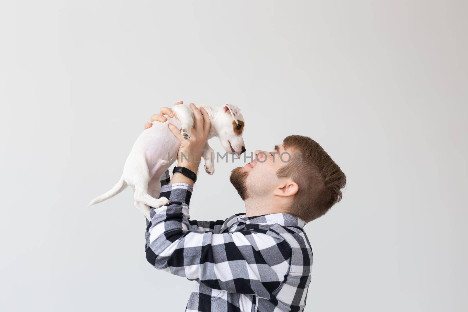 people, pets and animals concept - young man holding jack russell terrier puppy on white background with copy space.