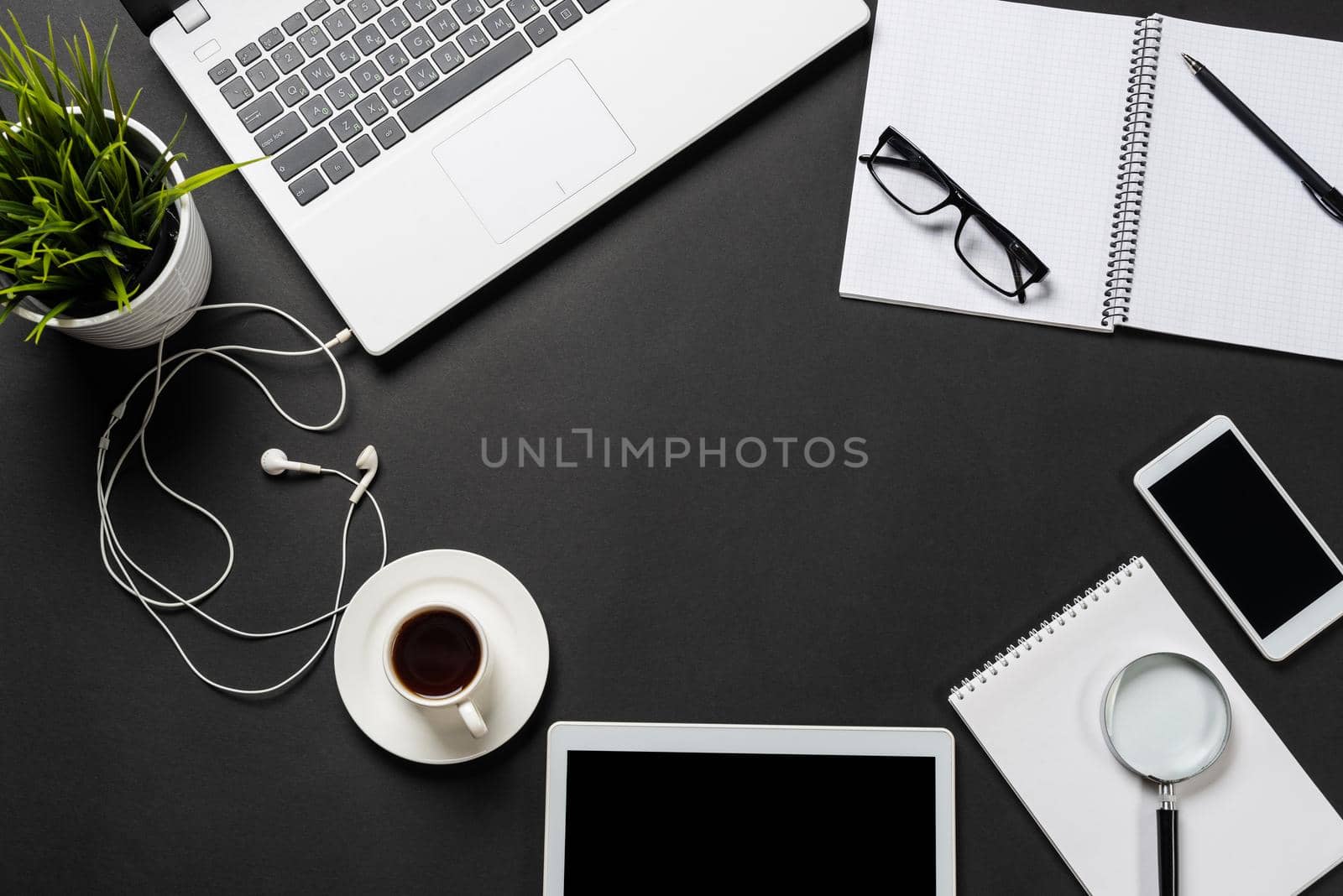 Top view of office workplace with digital gadgets. Flat lay black surface with laptop, green plant and cup of coffee. Top view coworking workspace with copy space. Digital technology and mobility.