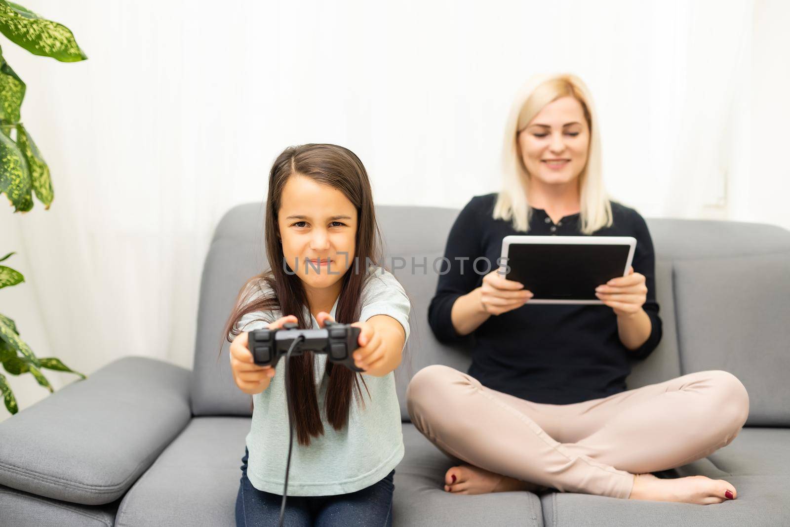 good relationship cute little girl with young mother using joystick playing video game sitting together in living room enjoying family holiday. by Andelov13