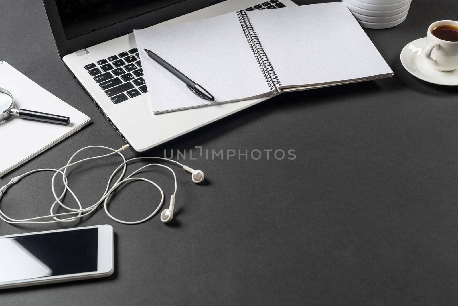 Still life of office workplace with laptop and cup of coffee. Flat lay black surface with computer and open blank notebook. Paperwork, audit and accounting. Top view modern workspace with gadgets