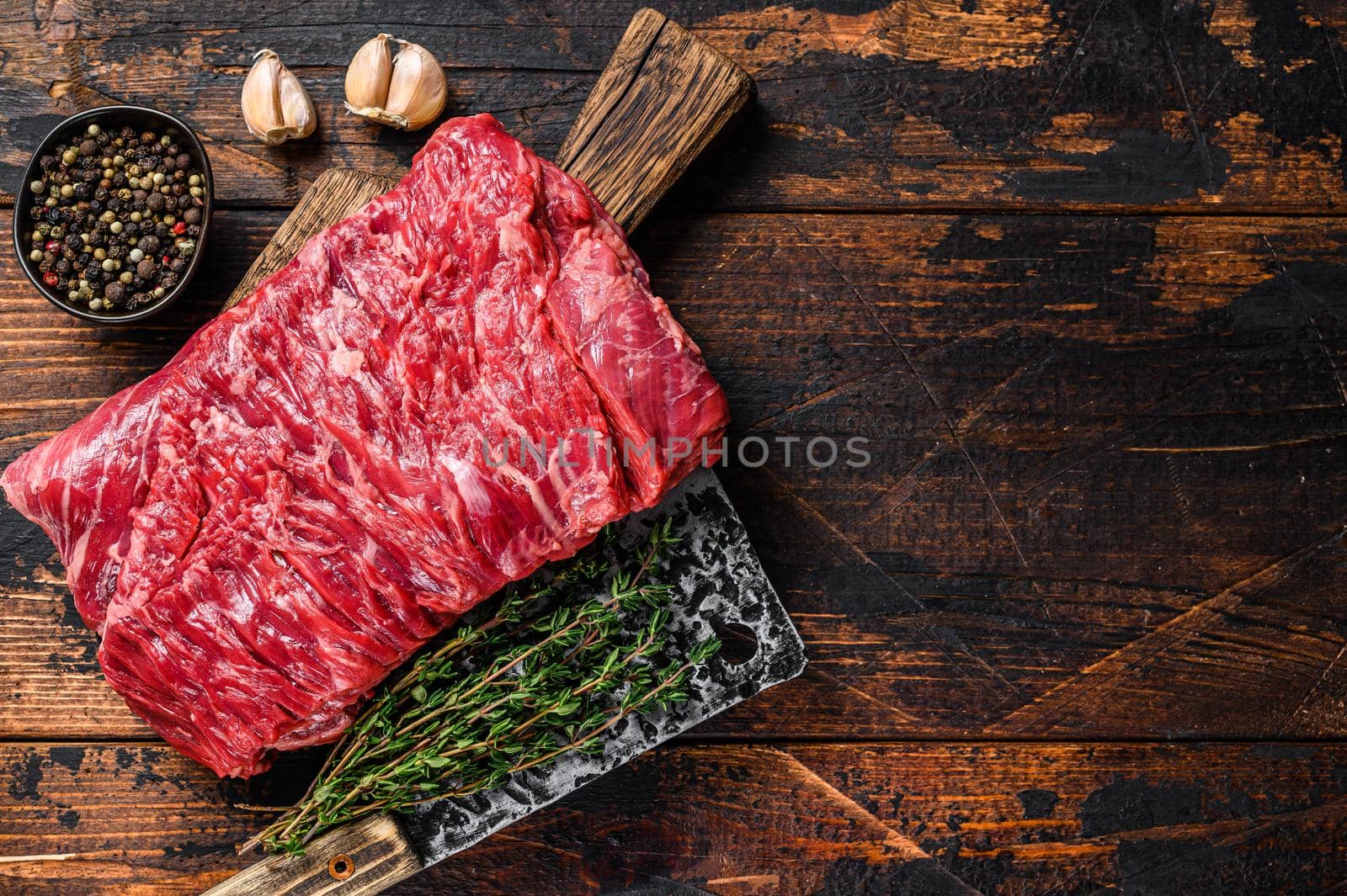 Big piece of raw beef brisket cut meat with herbs and butcher cleaver. Dark wooden background. Top view. Copy space by Composter