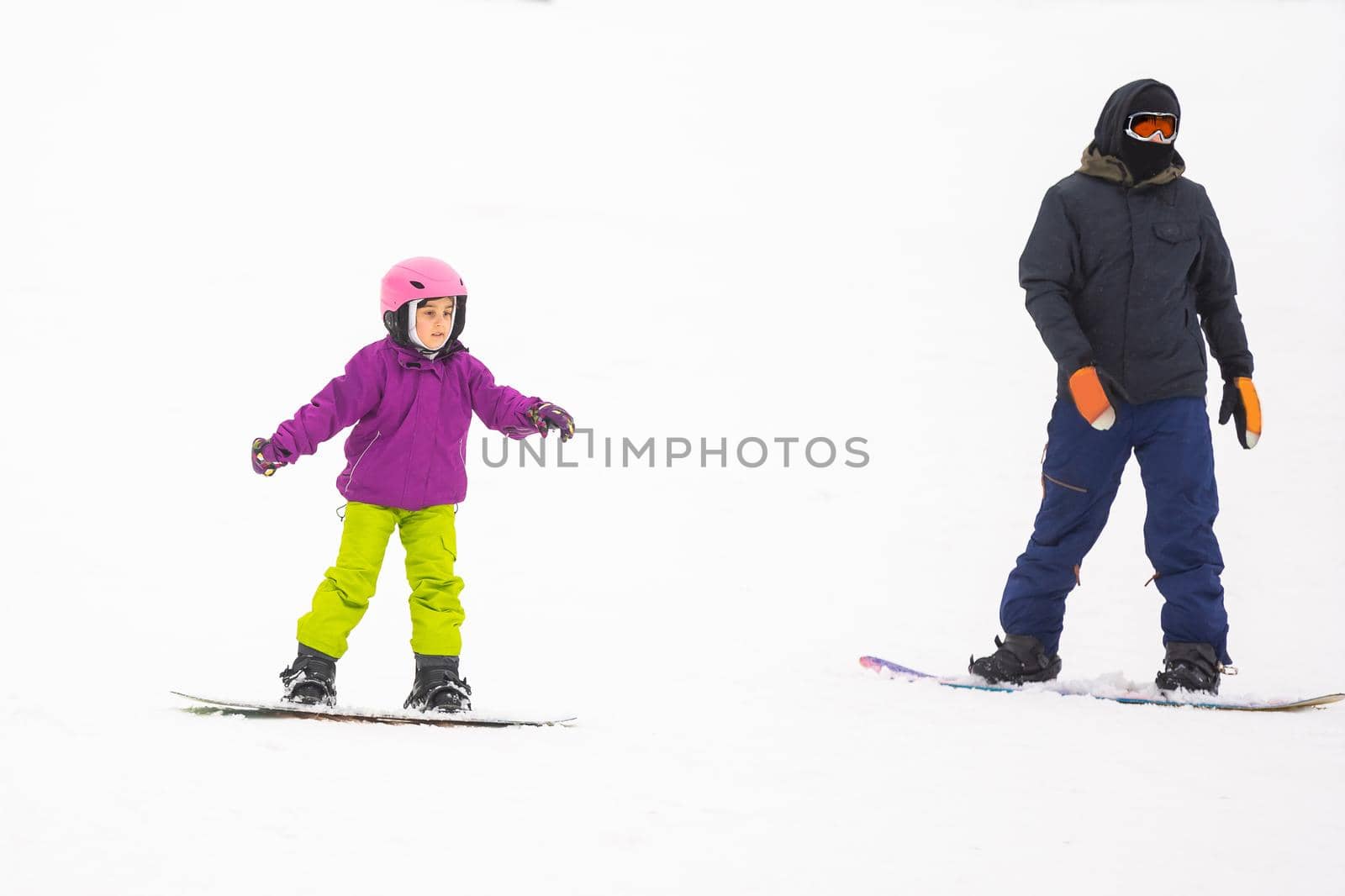 Instructors teach a child on a snow slope to snowboard