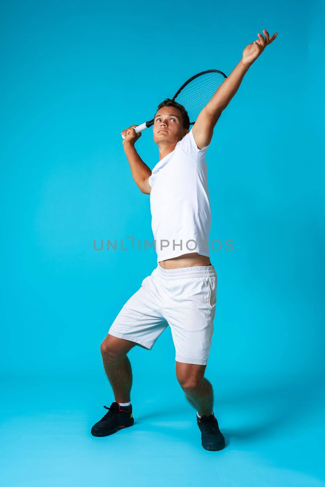 Full length studio portrait of a tennis player man on blue background close up