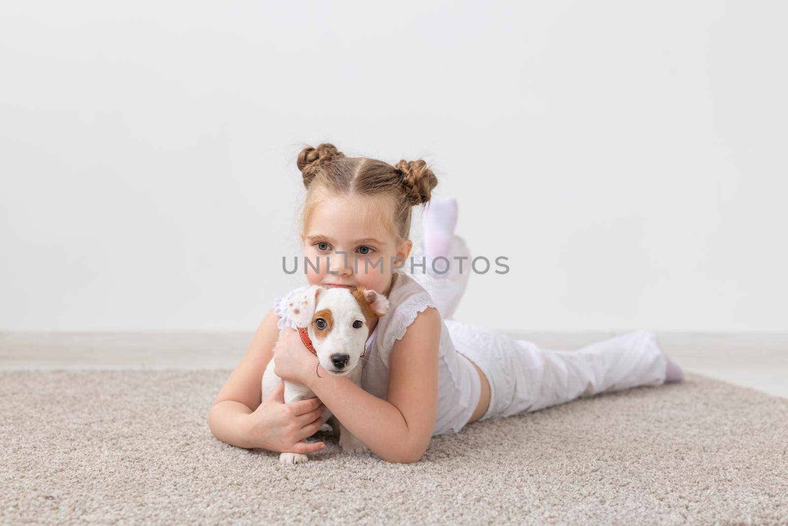 people, children and pets concept - little child girl lying on the floor with cute puppy.