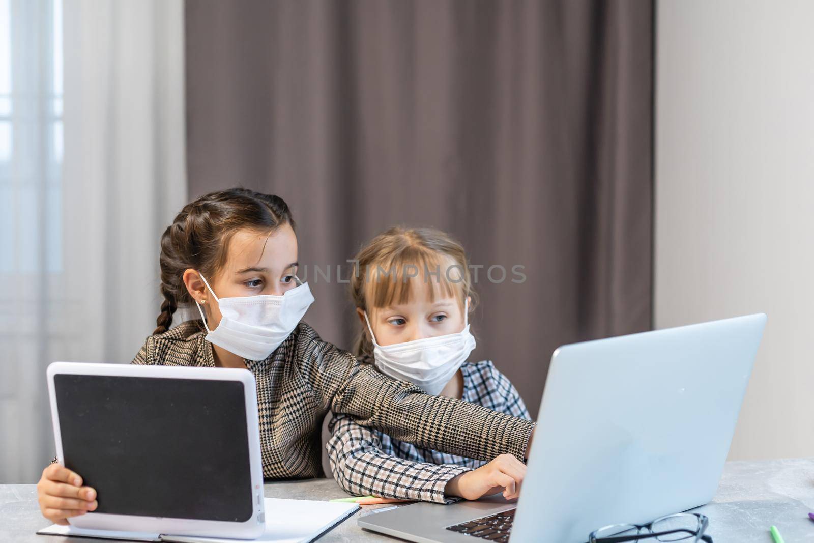 Distance Learning. School Girls At Laptop Wearing Mask Studying Online Sitting at the table at home by Andelov13