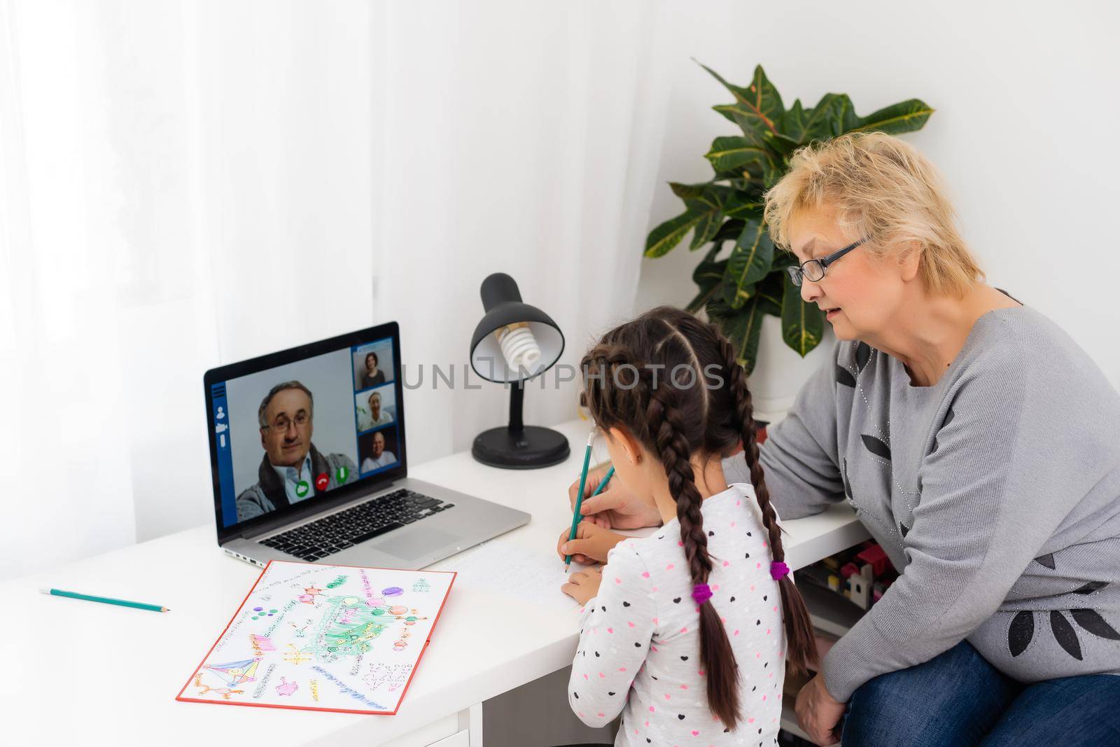 Cute and happy little girl child using laptop computer with her grandma, studying through online e-learning system.