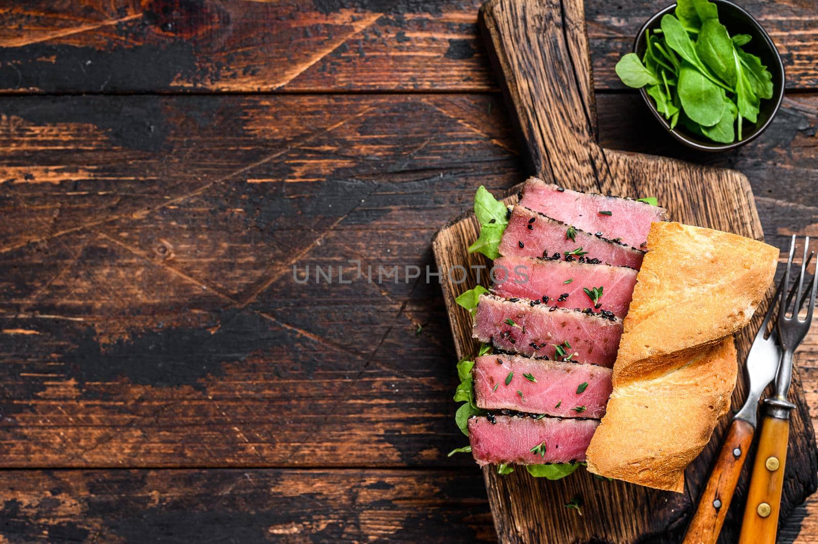 Grilled Ahi Tuna Steak and Avocado Sandwich with arugula on a cutting board. Dark wooden background. Top view. Copy space.