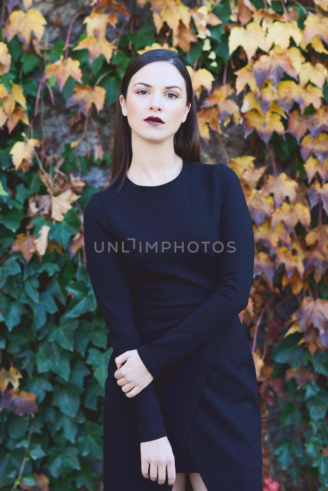 Beautiful young woman, model of fashion, wearing black dress in urban background with autumn colors. Very straight hair styling