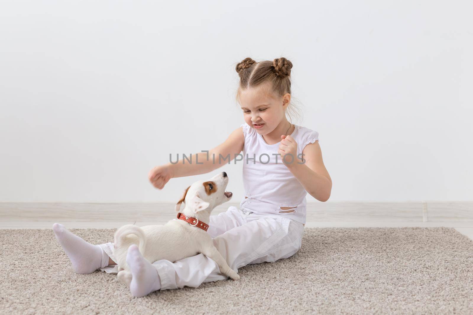 Children, pets and dogs concept - Child girl dressed in pajamas sitting on the floor and playing with puppy.