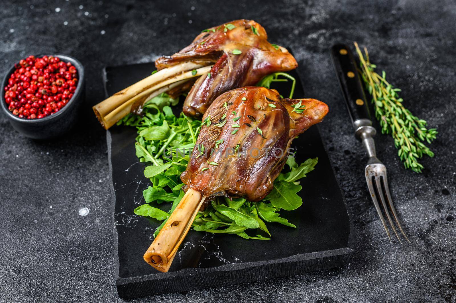 Stew goat Shanks on a marble board with arugula. Black background. Top view by Composter