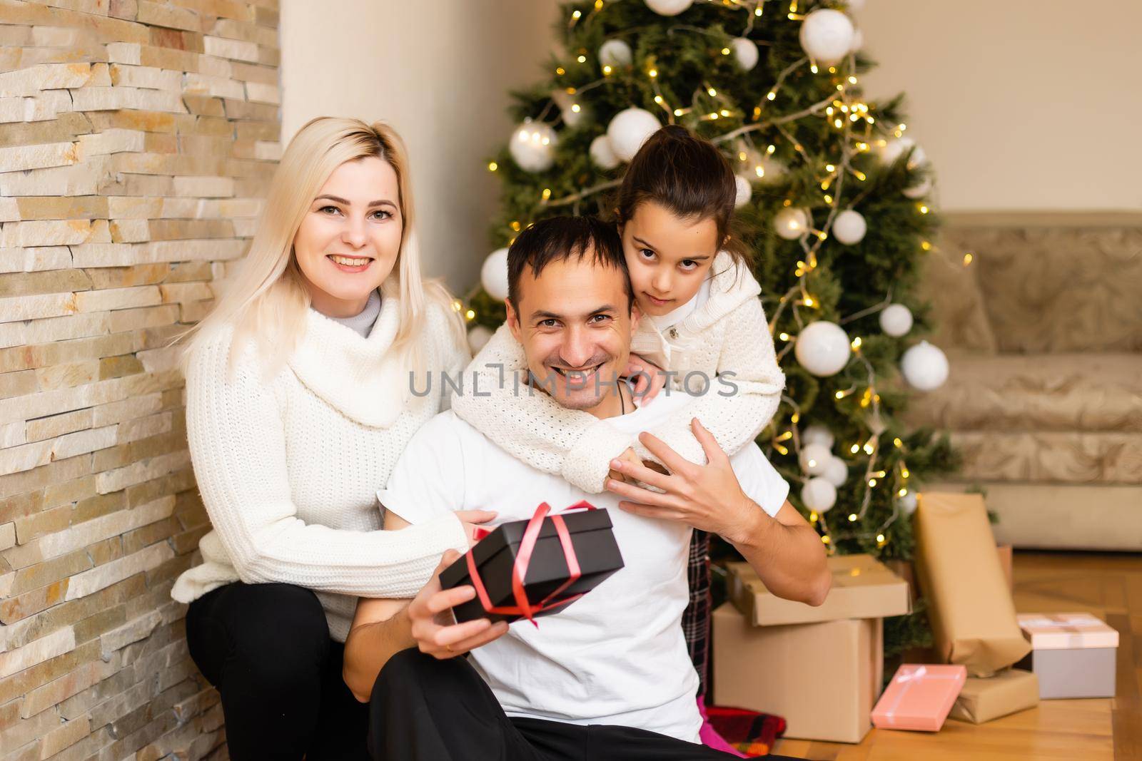 family, holidays and people - smiling mother, father and little girl over christmas tree lights background
