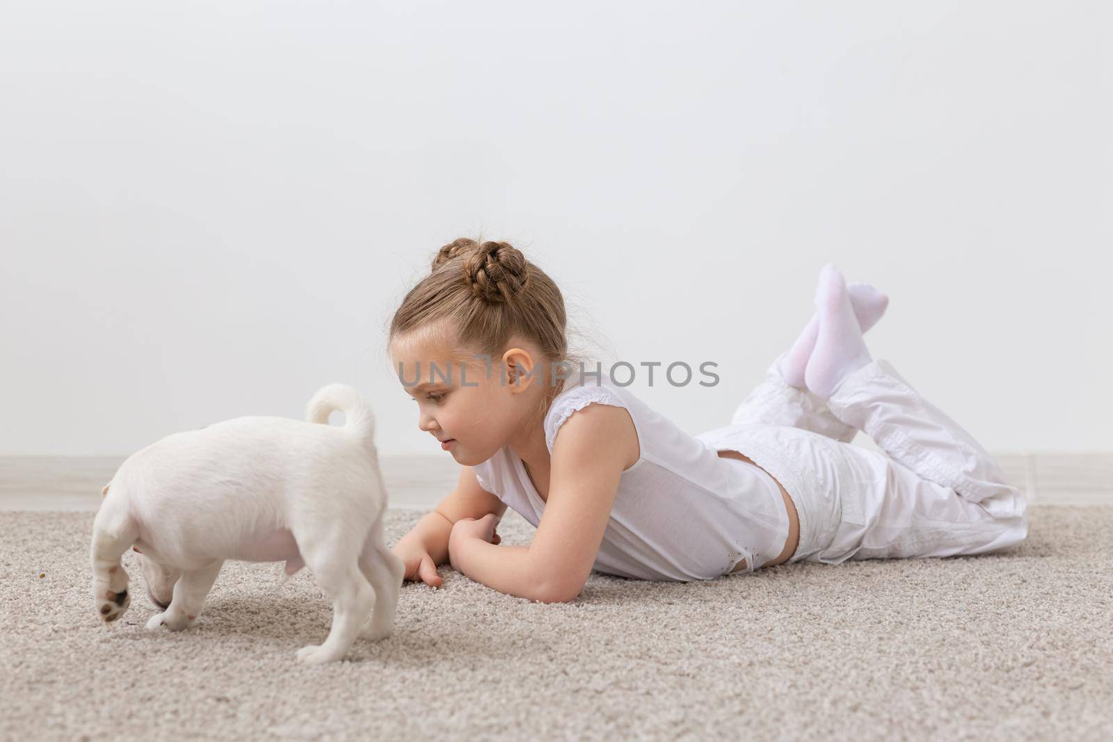 people, children and pets concept - little child girl lying on the floor with cute puppy.