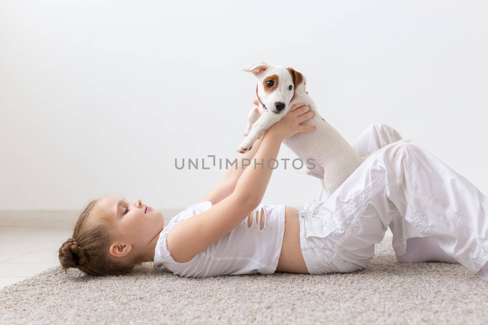 People, pets and animal concept - Little girl sitting on the floor over white background and holding puppy Jack Russell Terrier by Satura86
