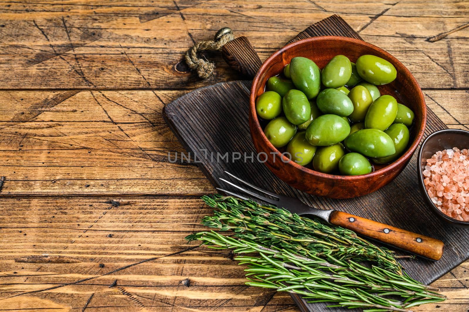 Marinated Green big olives in wooden bowl with oil. wooden background. Top view. Copy space by Composter