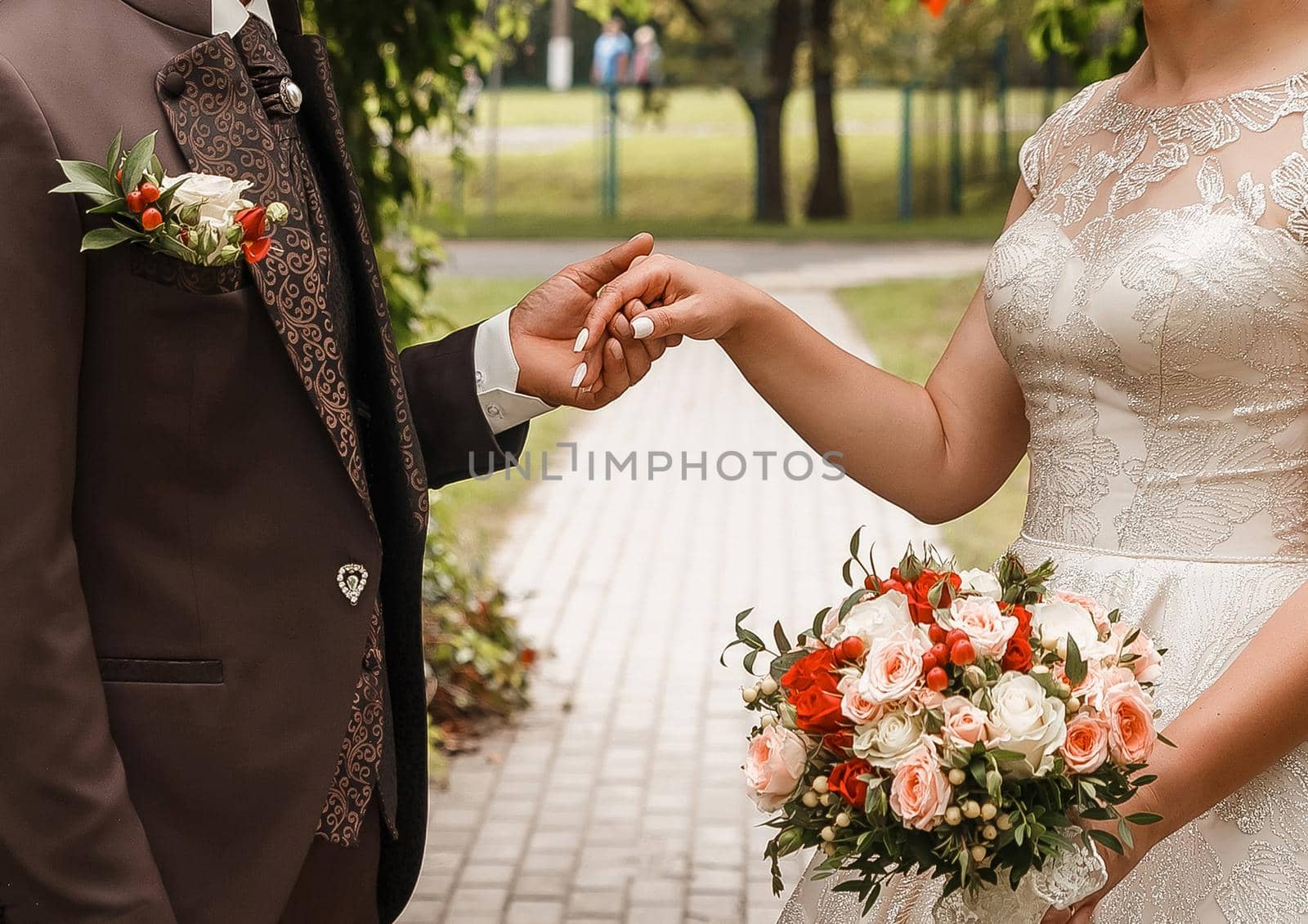 The groom in a brown suit holds the bride's hand with a wedding bouquet.
