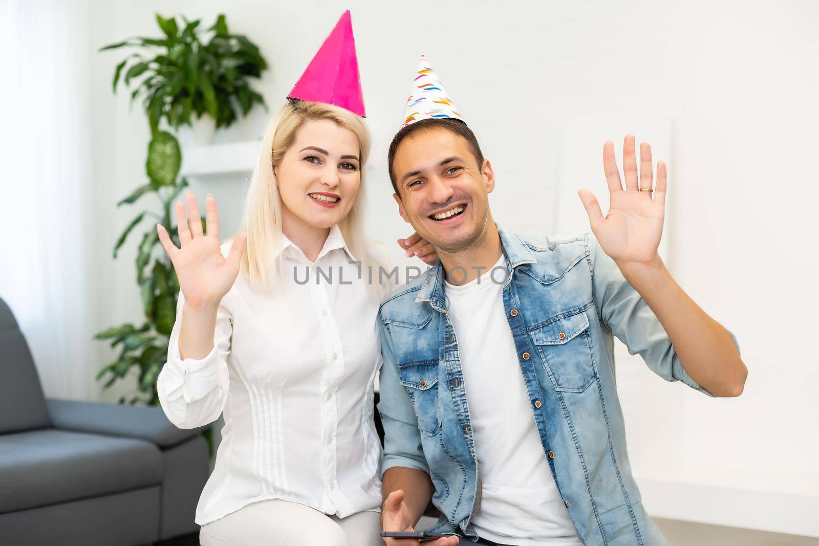 Young couple or friends in party hats having fun virtual celebration via video call.