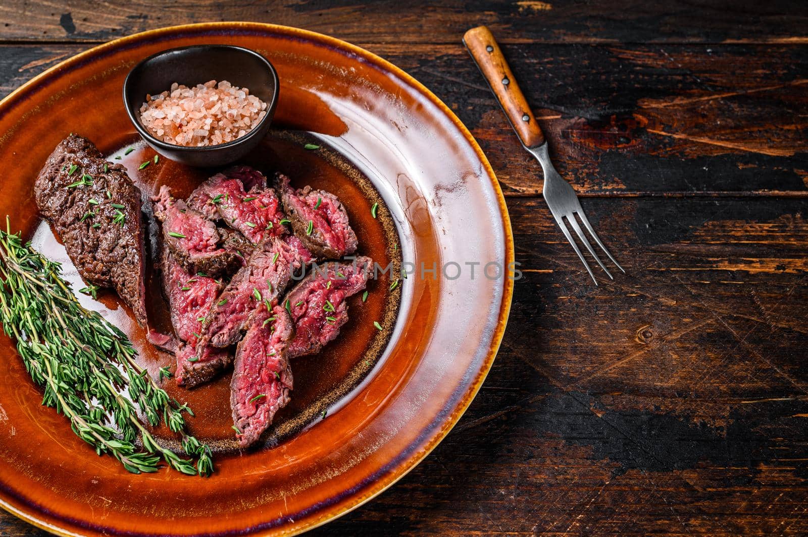 Medium rare Sliced grilled Onglet Hanging Tender meat beef steak on a plate. Dark wooden background. Top view. Copy space.