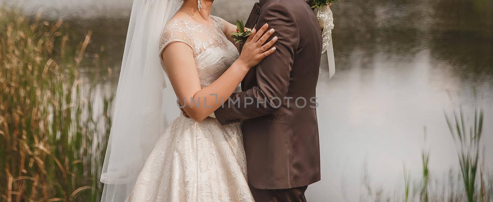 The bride put her hand on the groom's shoulder in a brown suit outdoor.