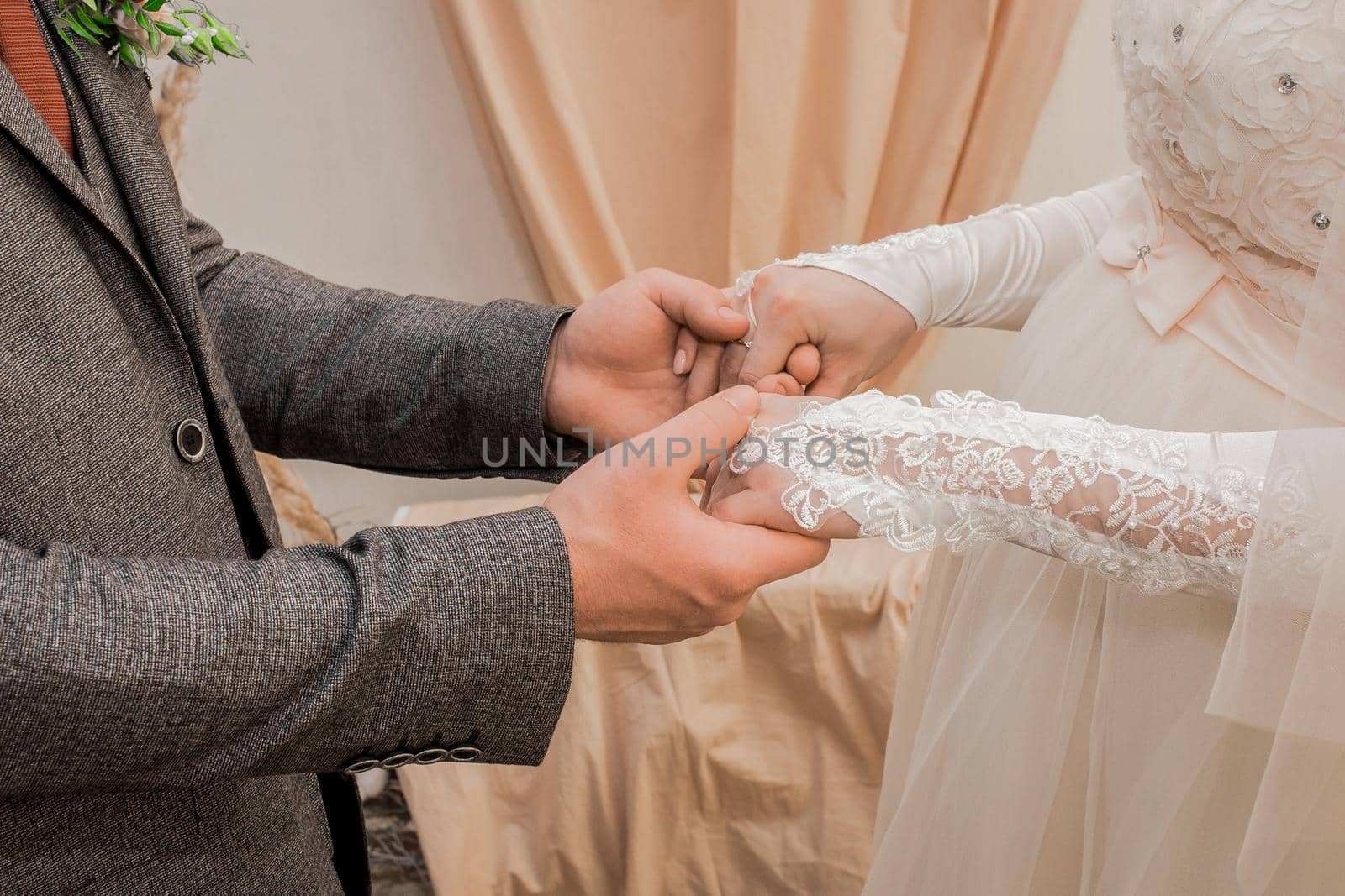 Male groom's hands hold bride's hands in wedding gloves.