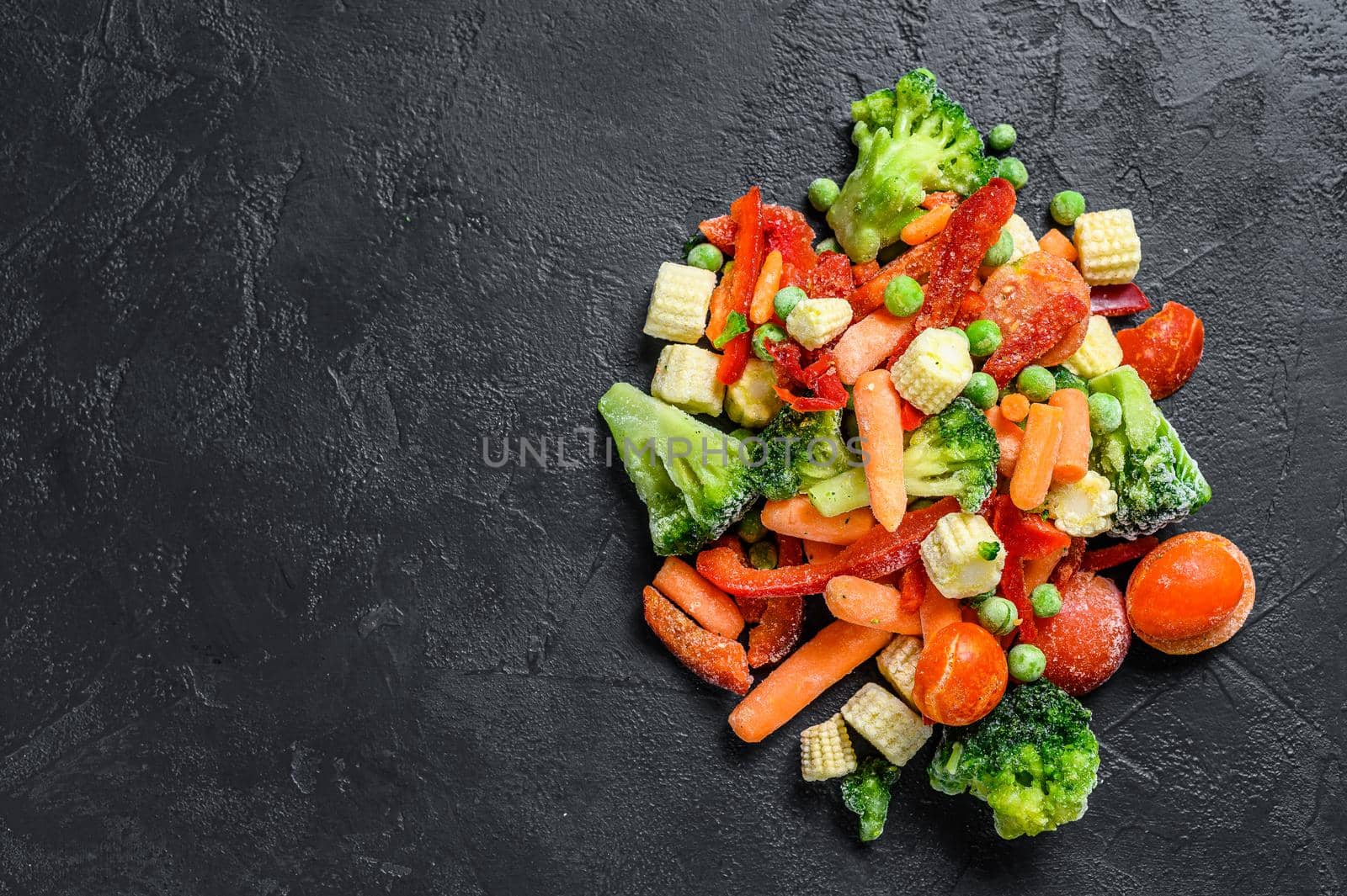 Frozen cold sliced Vegetables, broccoli, sweet peppers, tomatoes, carrots, peas and corn. Black background. top view. Copy space.