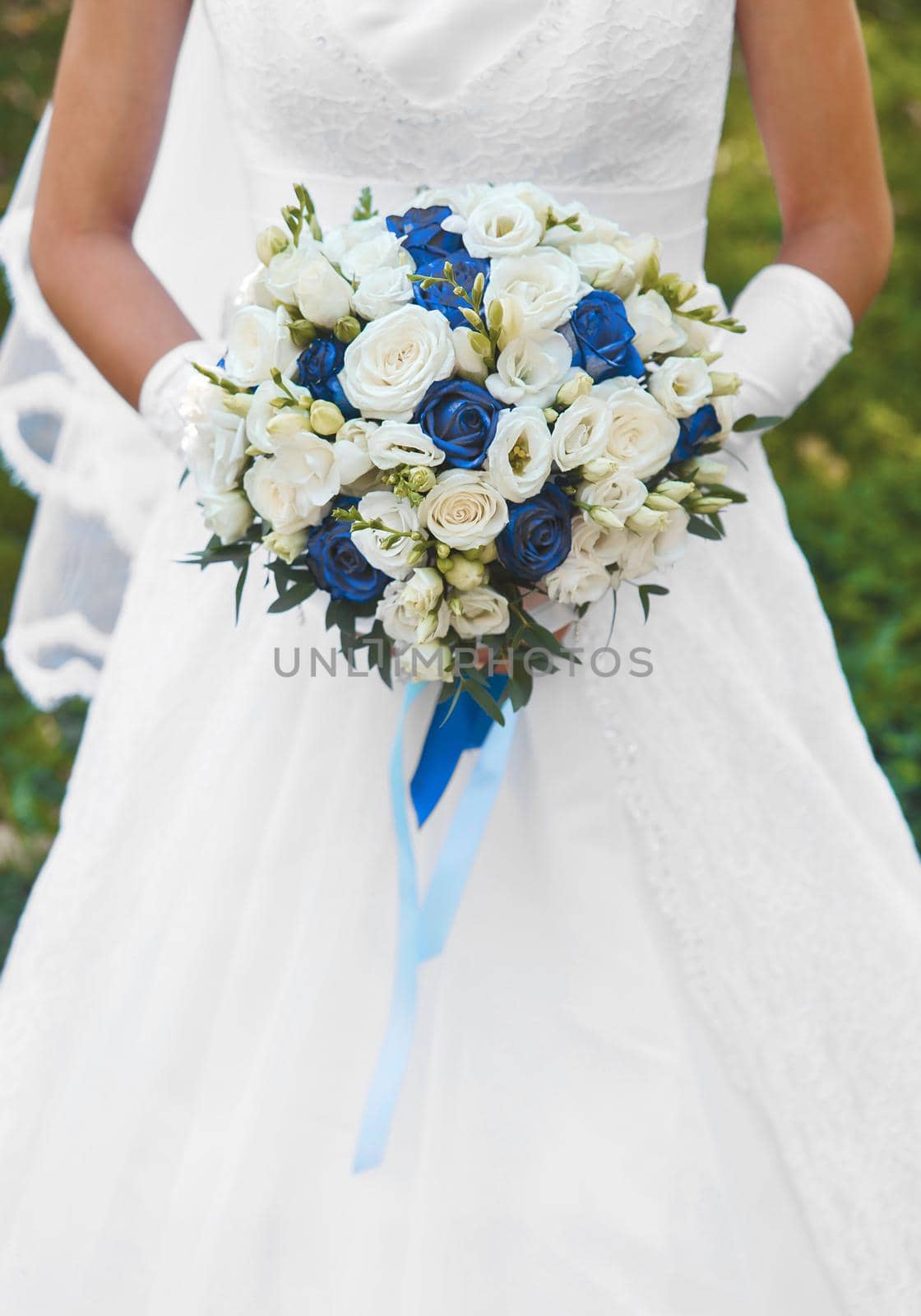Bride in white wedding dress holds a bouquet of flowers white and blue roses close up.