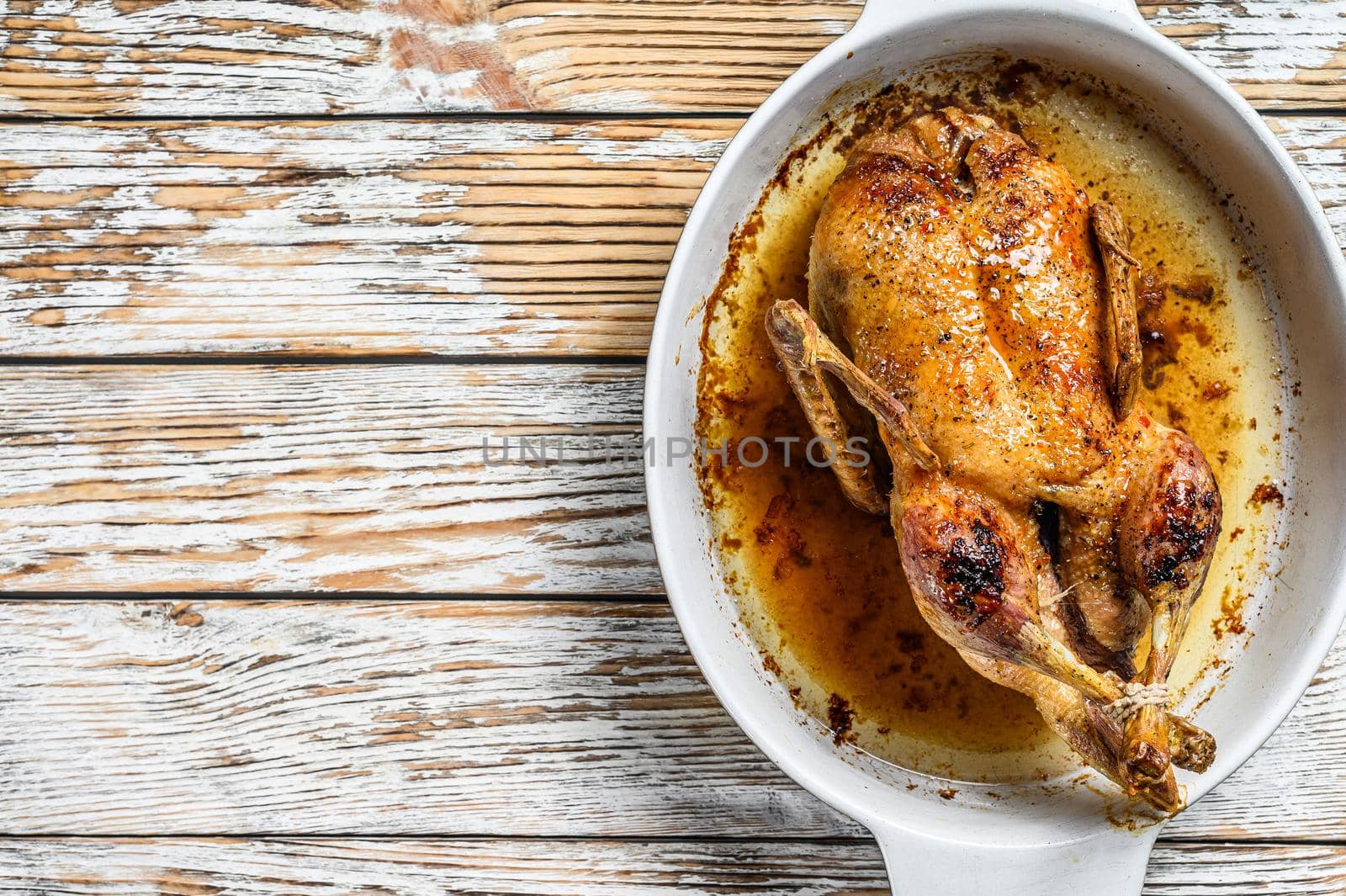 Baked whole farm duck in a baking dish. White wooden background. Top view. Space for text by Composter