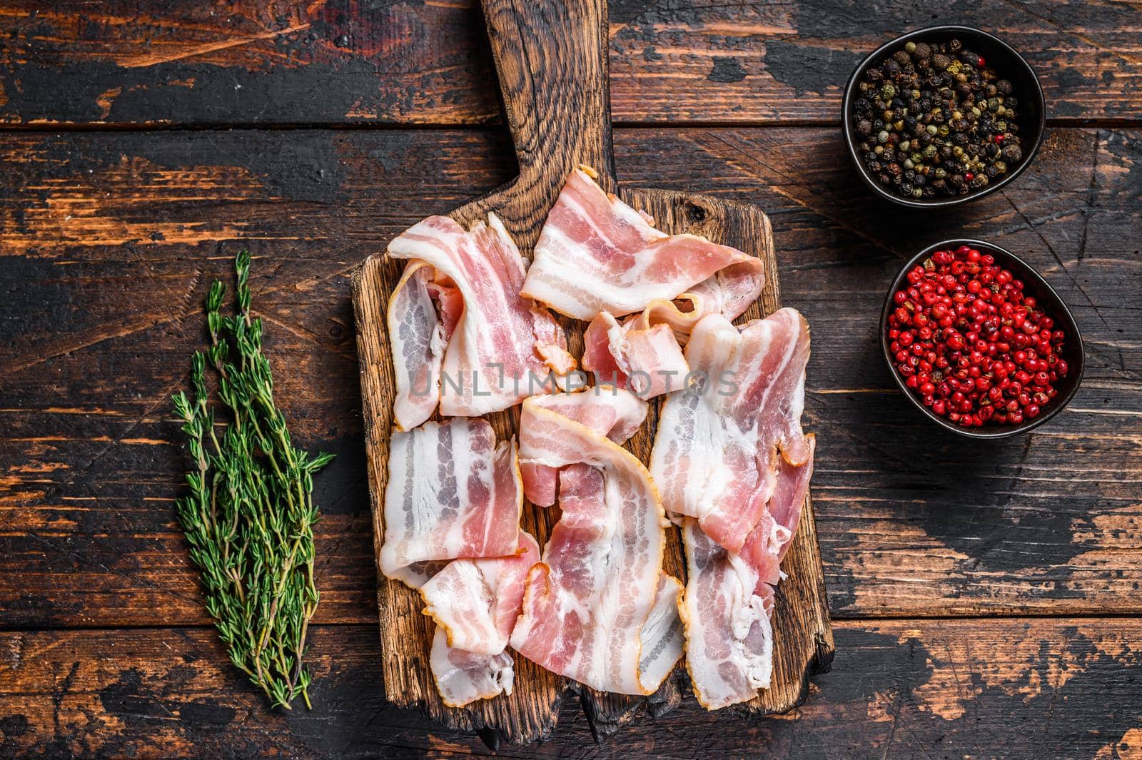 Raw pork bacon meat slices on a wooden cutting board. Dark wooden background. Top view by Composter